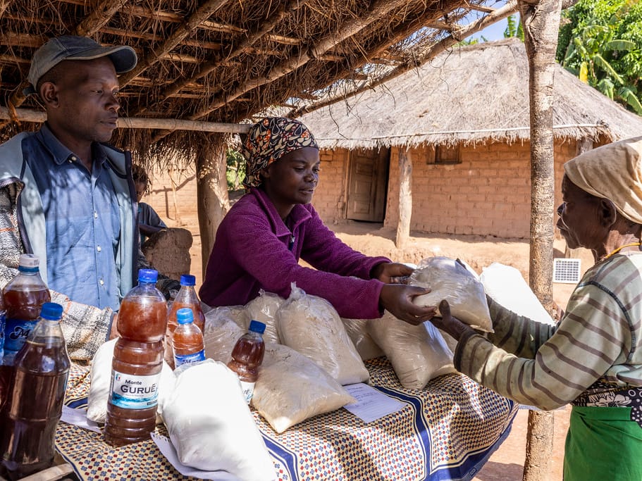 A vendor at a village food stall handing a bag of flour to a customer